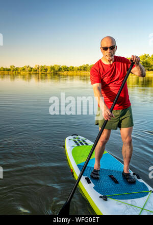 Ältere Erwachsene Paddler ist Paddeln aufblasbare Stand up paddleboard auf einem ruhigen See in Colorado. Stockfoto
