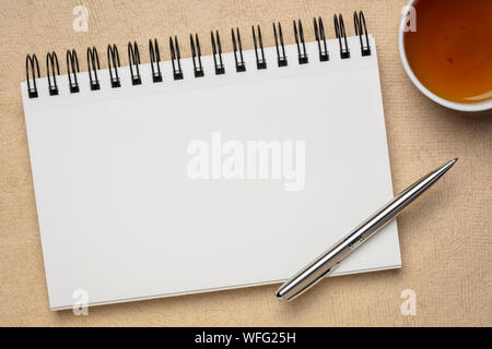 Leere Spirale Art Skizzenbuch gegen strukturierte Rinde Papier mit einer Tasse Tee Stockfoto