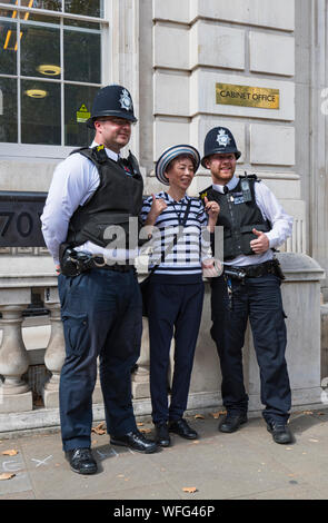 Paar Metropolitan Police Officers für Fotos mit Touristen außerhalb des Cabinet Office in Whitehall, Westminster, London, UK posieren. Polizisten. Stockfoto