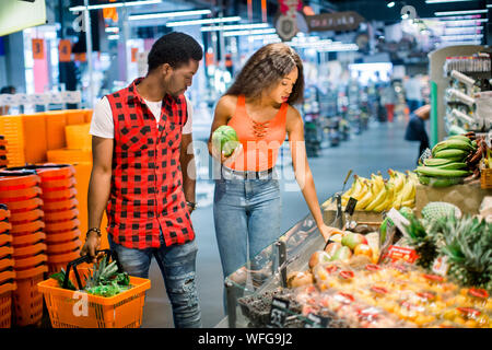 Lächelnd afrikanische amerikanische Paar mit Einkaufswagen mit Obst und Gemüse im Supermarkt. Stockfoto