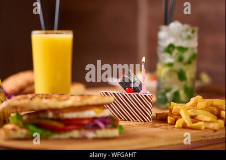 Fast food Tabelle für die Gesellschaft von Freunden serviert. Burger, Pommes und Getränke an Geburtstag serviert. Kinder geburtstag Zusammensetzung von Lebensmitteln, die mit Kuchen mit Stockfoto