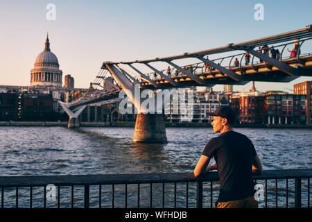Junger Mann auf Riverside gegen urban skyline. Kontemplation bei Sonnenuntergang. London, Vereinigtes Königreich.