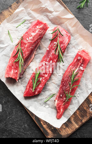 New York Strip Steak mit Salz und Rosmarin auf schwarzen Hintergrund, Ansicht von oben, aus der Nähe. Auch rohes Rindfleisch strip Steaks. Stockfoto