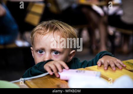 18 Monate groß schaut in die Kamera, als er gefangen, die versuchen, ein Power Bank w-/Ladekabel Kabel wie seine Mutter zu greifen, genießt die Zeit im Café mit neuen Baby auf Händen. Stockfoto