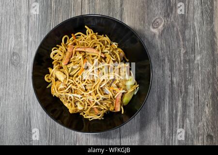 Schwarzes Schüssel mit einer Portion Huhn Lo Mein Nudeln platziert und auf eine strukturierte Holztisch isoliert. Stockfoto