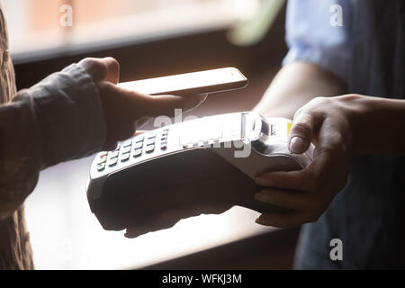 Weibliche Kunden holding Handy in der Nähe von NFC-Terminal eine Zahlung. Stockfoto