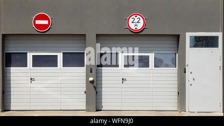 Vorderansicht bei zwei geschlossene Weiße garage Tore und eine Eingangstür, grau Formteile Wände und Verkehrszeichen auf es Stockfoto