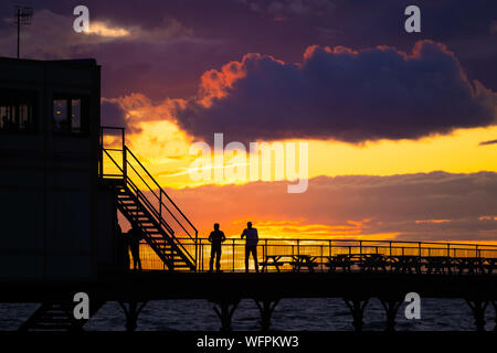 Aberystwyth Wales UK, Samstag, 31. August 2019 Leute stehen an der viktorianischen Badeort von Aberystwyth Pier sind silhouetted, als Sie den letzten Sonnenuntergang der 2019 Sommer beobachten. Morgen, am 1. September ist der erste Tag der meteorologische Herbst. Foto Keith Morris/Alamy Live Neue Stockfoto