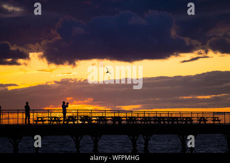 Aberystwyth Wales UK, Samstag, 31. August 2019 Leute stehen an der viktorianischen Badeort von Aberystwyth Pier sind silhouetted, als Sie den letzten Sonnenuntergang der 2019 Sommer beobachten. Morgen, am 1. September ist der erste Tag der meteorologische Herbst. Foto Keith Morris/Alamy Live Neue Stockfoto