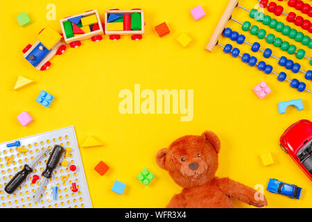 Kinder Spielzeug Hintergrund. Teddybär, Holzeisenbahn, bunte Bausteine, Spielzeug tools Kit, Autos, Abacus auf gelbem Hintergrund Stockfoto