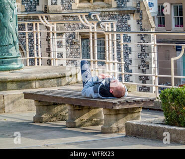 Norwich, Norfolk, Großbritannien - 31 August 2019. Junge männliche schlafen Sie ein Kater von der Nacht zuvor auf einer konkreten Bank in einem Stadtpark Stockfoto