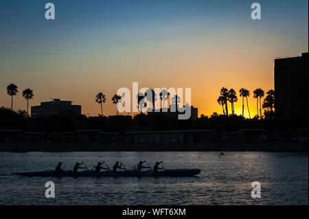 Silhouette einer Gruppe, die bei Sonnenuntergang im Hafen von Marina Del Rey in Los Angeles, CA, mit einem Auslegerkanu paddelt. Stockfoto