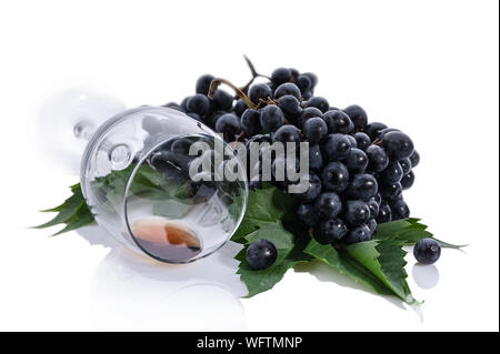 Trauben von schwarzen Trauben mit Blättern und einem Glas Wein auf weißem Hintergrund Stockfoto