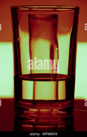 Ein Glas Wasser bricht Licht von einem bunten Hintergrund Stockfoto