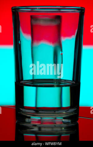 Ein Glas Wasser bricht Licht von einem bunten Hintergrund Stockfoto