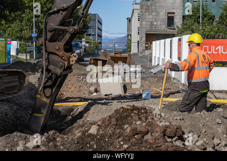 Reykjavik, Island - August 08, 2019: Ein männlicher Konstruktor tragen Helm ständigen Suchen eine große pneumatische Hammer, die in der Straße. Stockfoto