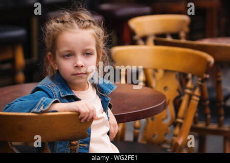 Modische kleines Schulmädchen auf der Terrasse des Restaurants zu sitzen. Sie ist melancholing. Text Raum Stockfoto