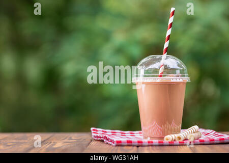 Schokolade Milchshake in Einweg Plastikbecher mit waffelröllchen auf hölzernen Tisch im Freien Stockfoto