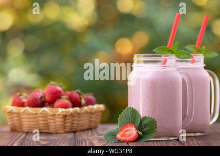 Strawberry Smoothie in Mason jars und frische reife Beeren im Korb auf hölzernen Tisch im Freien Stockfoto
