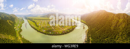 Panoramablick auf den Fluss, ein kleines Dorf vor der Bergkette. Nationalpark in der Republik Altai. Antenne Weitwinkel drone Blick auf den Fluss Stockfoto