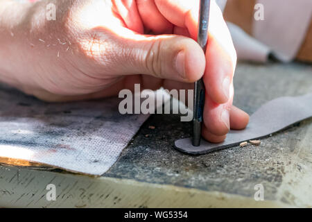 Männliche Schuster Hände, ein Loch in ein Stück Leder, mit einem Schlag. Stockfoto