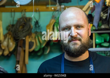 Porträt einer kahlen mand mit Bart, Schuhmacher, die Kamera in seiner Werkstatt. Stockfoto