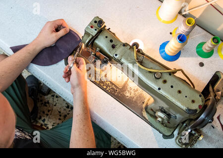 Blick von oben auf einen männlichen Schuster schneiden ein thread nach dem nähen Leder mit einer alten Nähmaschine. Stockfoto