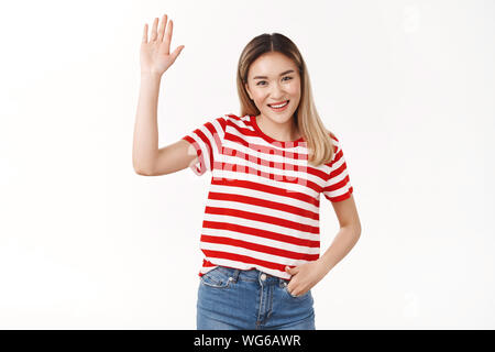 Hey Freunde wie hängen. Freundlich ausgehende Kontaktfreudig cute Asian blonde Mädchen anheben Hand waving palm Hi Hello Geste lächelnd weitgehend glücklich einführen Stockfoto