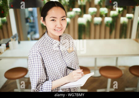 Hohen winkel Portrait von lächelnden Asiatische Kellnerin auf Kamera während der Bestellung im Cafe, kopieren Raum Stockfoto