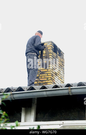 Schornsteinfeger bei der Arbeit auf einem Dach mit einem gelben Stein Kamin Stockfoto