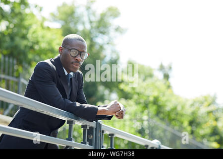 Portrait von stilvollen Afrikaner - Mann mit Anzug und Brille posing lehnte sich auf Geländer draußen im Park, Kopie Raum Stockfoto