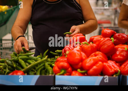 Details eines Mannes die Wahl Hot Paprika (süße Paprika auch auf dem Regal) auf das Obst und Gemüse Gang in einem Geschäft Stockfoto