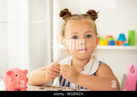 Süße kleine Mädchen Träume mit einem Sparschwein. Planung, um Geld zu sparen. Stockfoto