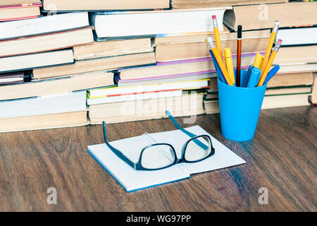 Stapel von alten Buch, Kugelschreiber und Bleistifte in Halter, geöffnet Notebook und Gläser. Bildung Konzept Hintergrund, viele Bücher Stapel mit Platz für Text kopieren Stockfoto