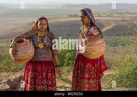 Zwei Ahir Frauen in traditionelle bunte Kleidung tragen von Wasser in einem Ton Kanne, tolle Rann von Kutch, Gujarat, Indien Stockfoto