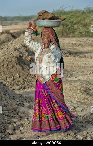 Fakirani Frau in traditionelle bunte Kleidung, die Erde auf ihrem Kopf für Straßenarbeiten, tolle Rann von Kutch, Gujarat, Indien Stockfoto