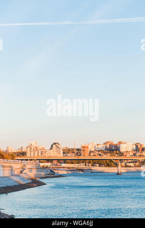 Wunderschöne Aussicht auf die Stadt über dem blauen breiten Fluß mit einer Brücke. Ein hohes Gebäude auf dem Himmel Hintergrund Stockfoto