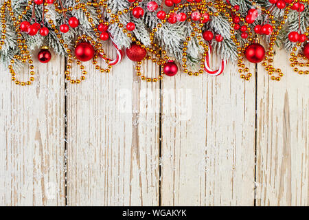 Weihnachten Zusammensetzung Grenze von rot Stechpalme Beeren, goldene Sterne, Garland, Kugeln und Grüne Tanne Zweig auf weißem Holz- Hintergrund. Minimale Xmas Stockfoto