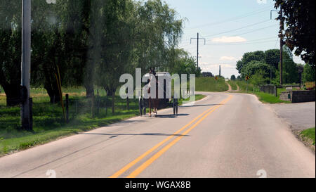 Blick auf einen amischen Pferd und Buggy hinunter die Straße an einem sonnigen Tag Stockfoto