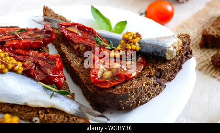 Lecker smorrebrod auf einem weißen Teller. Sandwiches mit schwarzem Roggenbrot, getrocknete Tomaten, gesalzene Sardellen, Senf. Stockfoto