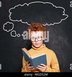 Kind Junge Lesen eines Buches auf Schule Schiefertafel Hintergrund mit leeren Rede wolken Blasen Stockfoto