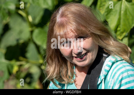 Ältere Frau stellt in einem Feld, lächelnd und sah Stockfoto