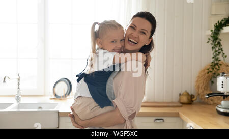Happy Mother Holding auf Händen entzückende Tochter im Vorschulalter in der Küche Stockfoto