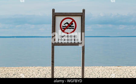 Ein großes Holz Schild am Strand liest Schwimmen mit einer ruhigen Bucht im Hintergrund verboten. Stockfoto