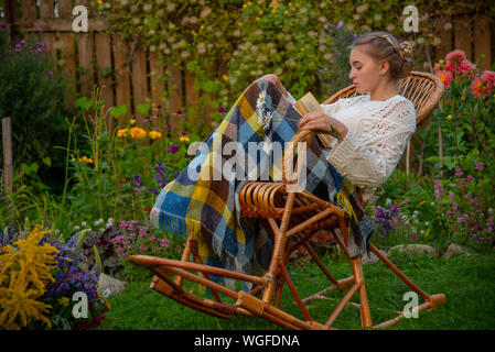 Schöne Mädchen in einem Rattan Schaukelstuhl mit einem Buch sitzen Stockfoto