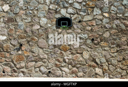 Ein Basketball Backboard, Rim und Netz unter der Mittagssonne, auf Mauerwerk im Freien montiert. Stockfoto