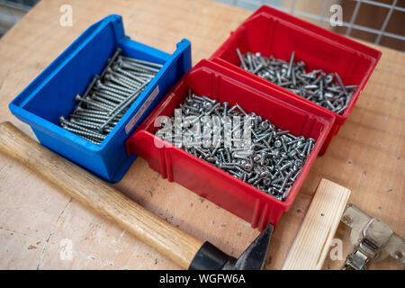 Auf der Tabelle sind verschiedene farbige Boxen mit Schrauben gefüllt und neben ihnen ist ein Hammer Stockfoto