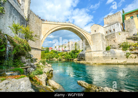 Ein kleiner Wasserfall an der Unterseite der Brücke von Mostar in Bosnien und Herzegowina als Touristen genießen den Blick auf das smaragdgrüne Wasser des Flusses Neretva Stockfoto