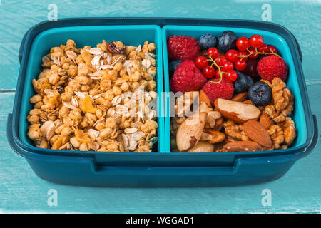 Gesunde Schule Lunch Box mit Müsli, Nüsse und Beeren gesundes Frühstück auf Blau Holz- Hintergrund zu machen. Nach oben Schließen Stockfoto