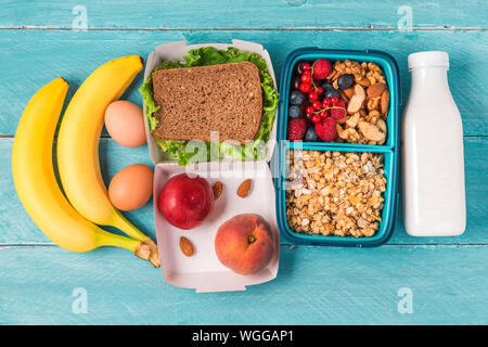 Gesundes Mittagessen Boxen mit Sandwich, Müsli, Gemüse, Nüsse, Beeren, Banane, Eier, Pfirsiche und Joghurt auf blauem Hintergrund. top View Stockfoto